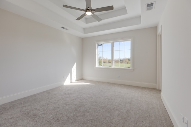 empty room with ceiling fan, light colored carpet, and a raised ceiling