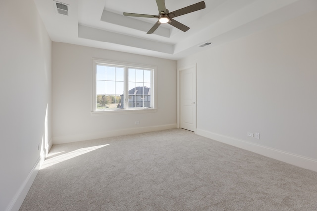 empty room featuring light carpet, a tray ceiling, and ceiling fan