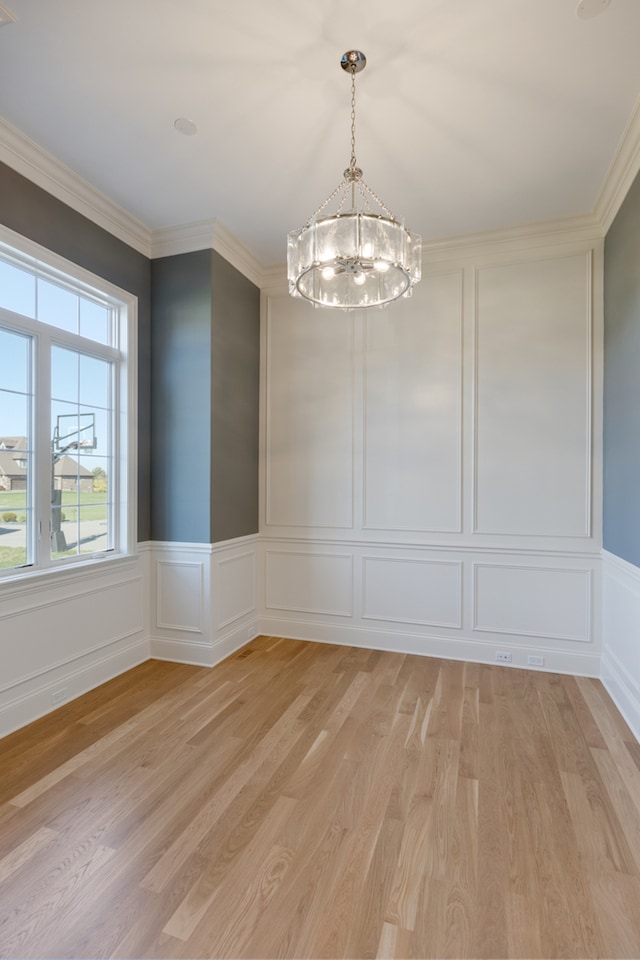 unfurnished dining area with a notable chandelier, ornamental molding, and light wood-type flooring