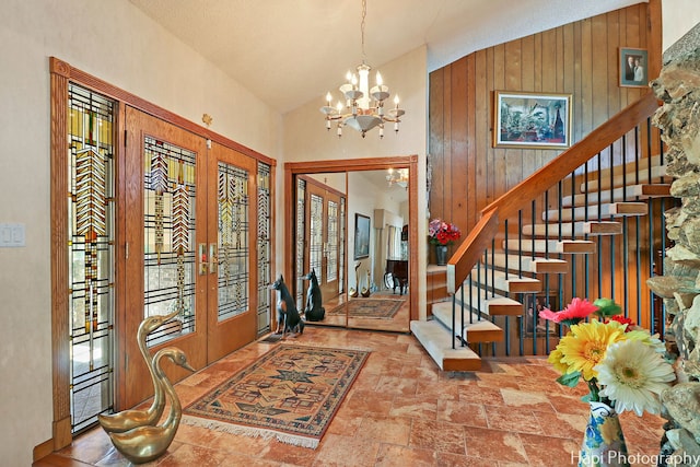 foyer with french doors, high vaulted ceiling, a notable chandelier, and wooden walls