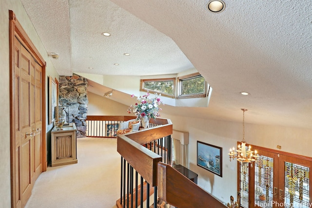 corridor with vaulted ceiling with skylight, a textured ceiling, a chandelier, and light carpet