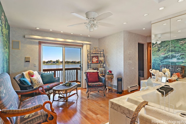 living room with a baseboard heating unit, ceiling fan, a water view, and hardwood / wood-style flooring