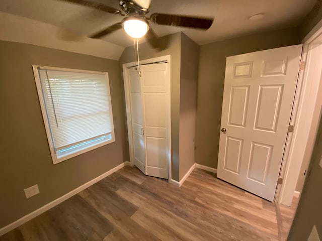 unfurnished bedroom with ceiling fan, hardwood / wood-style floors, multiple windows, a closet, and vaulted ceiling