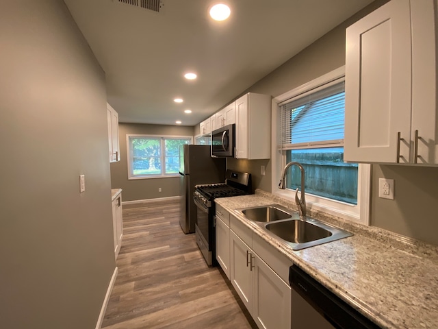 kitchen with light stone counters, white cabinetry, appliances with stainless steel finishes, sink, and light hardwood / wood-style flooring