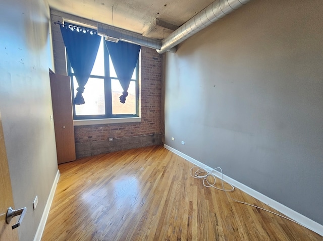 unfurnished room with brick wall and light hardwood / wood-style flooring