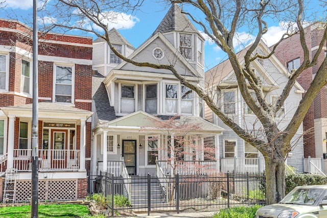 view of front of property featuring covered porch, roof with shingles, and a fenced front yard