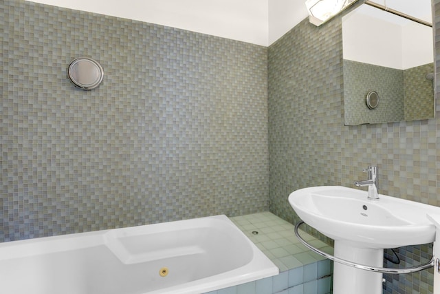 bathroom featuring a jetted tub, tile walls, and a sink