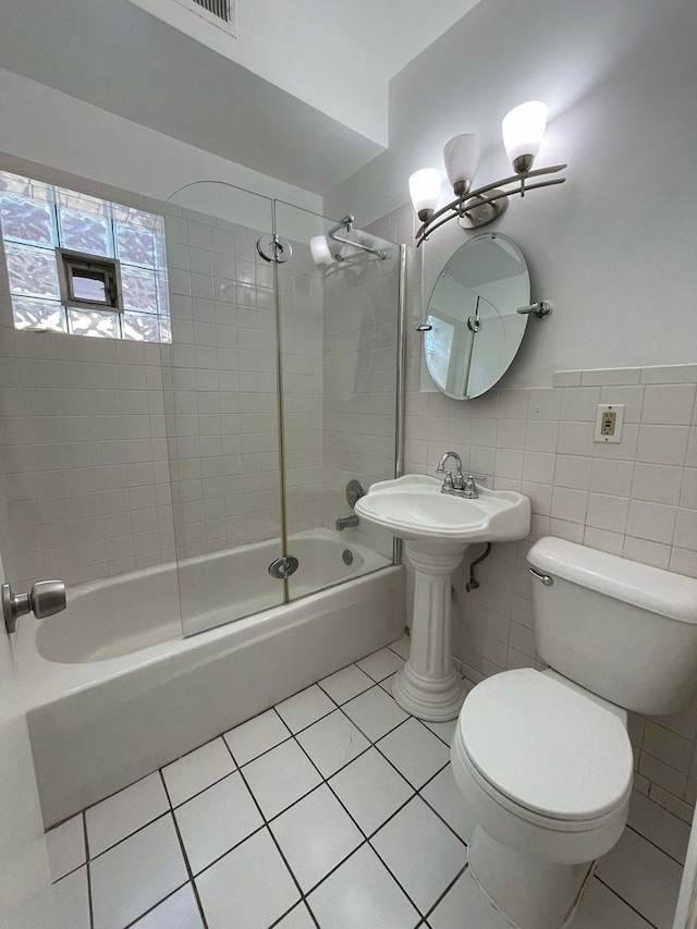 bathroom featuring toilet, tiled shower / bath combo, tile patterned flooring, and tile walls