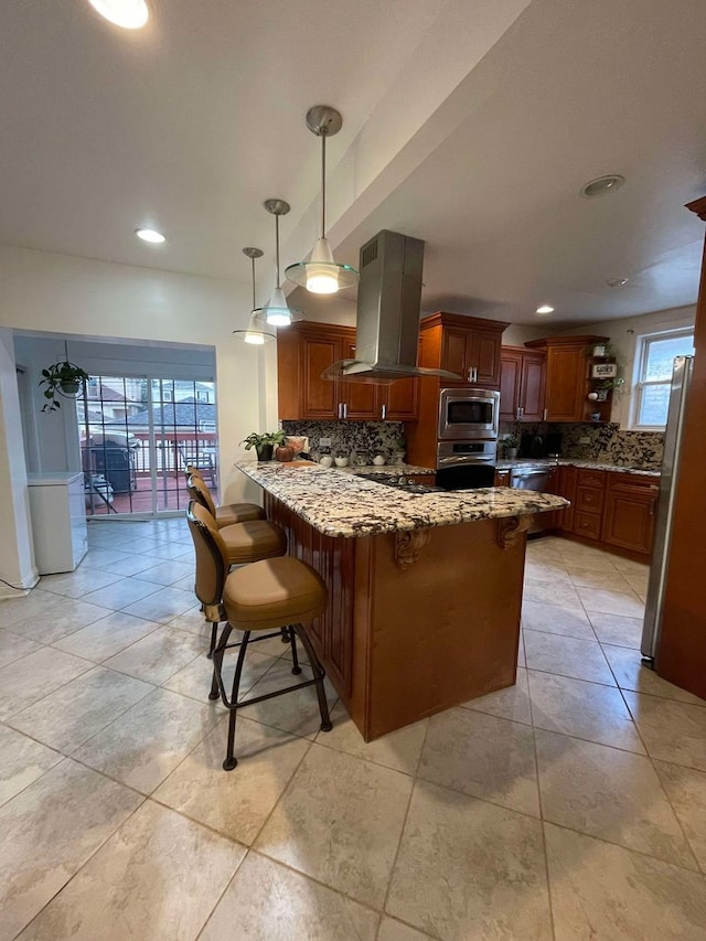 kitchen featuring appliances with stainless steel finishes, a kitchen bar, island range hood, backsplash, and kitchen peninsula