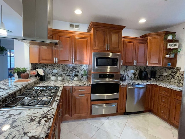 kitchen featuring appliances with stainless steel finishes, light tile patterned flooring, island range hood, light stone counters, and decorative backsplash