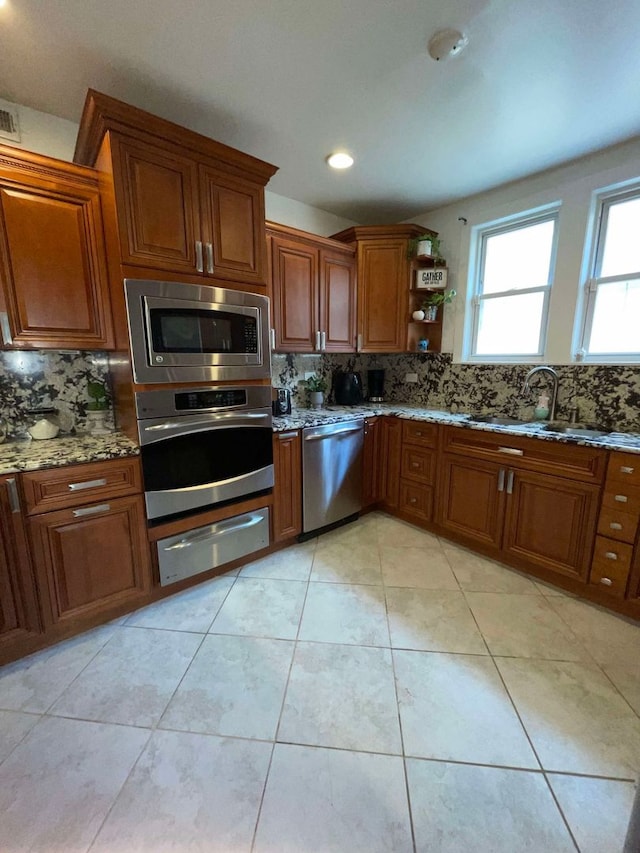 kitchen featuring sink, light tile patterned flooring, stainless steel appliances, light stone counters, and decorative backsplash