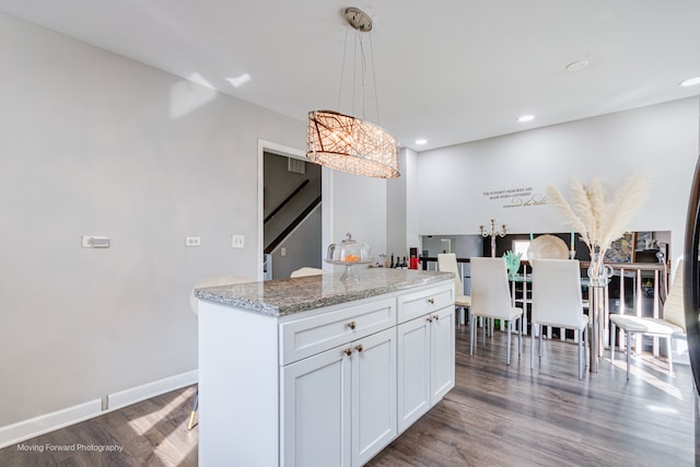 kitchen featuring a center island, hardwood / wood-style flooring, light stone countertops, decorative light fixtures, and white cabinetry