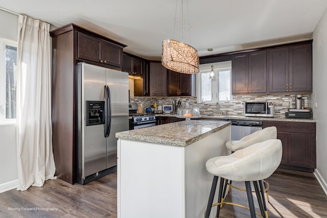 kitchen with tasteful backsplash, stainless steel appliances, decorative light fixtures, dark hardwood / wood-style floors, and a kitchen island