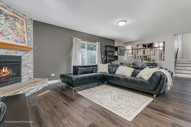 living room with a stone fireplace and dark wood-type flooring