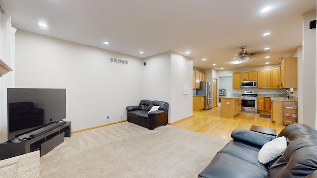 living room featuring light wood-type flooring, ceiling fan, and sink