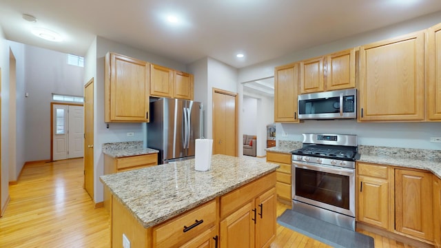 kitchen with stainless steel appliances, light stone countertops, light hardwood / wood-style flooring, and a center island