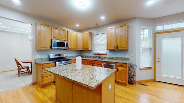 kitchen with sink, light stone counters, appliances with stainless steel finishes, a center island, and light wood-type flooring