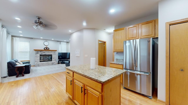 kitchen with a center island, ceiling fan, stainless steel refrigerator, light stone countertops, and light wood-type flooring