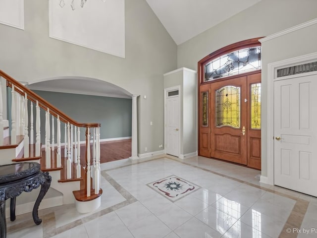 foyer entrance with crown molding, ornate columns, high vaulted ceiling, and light tile patterned floors