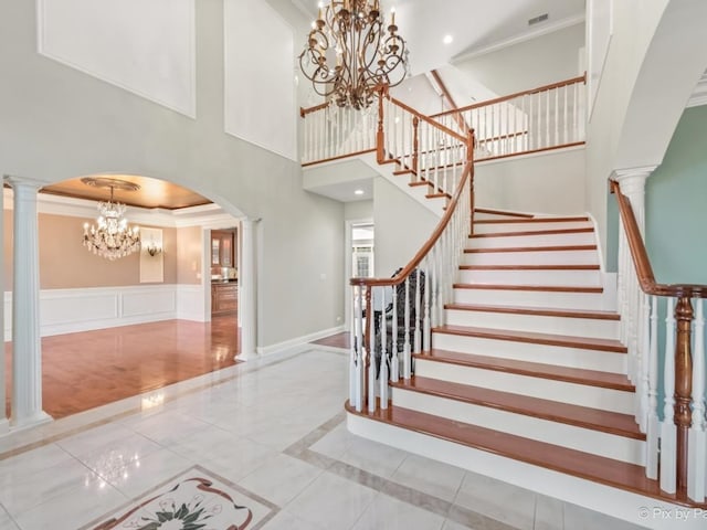 staircase featuring a towering ceiling, ornamental molding, tile patterned floors, and decorative columns