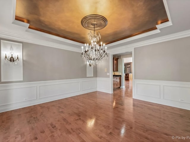 unfurnished dining area with crown molding, a raised ceiling, and wood-type flooring