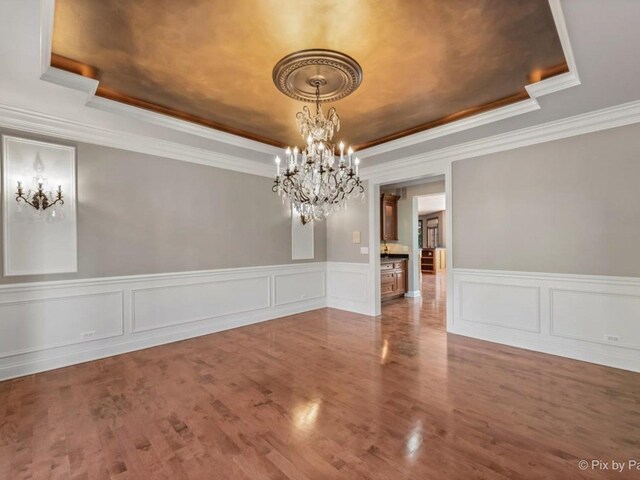 239 Indian Trail Rd, North Barrington, IL 60010 - unfurnished dining area with a raised ceiling, a chandelier, ornamental molding, wood finished floors, and a wainscoted wall