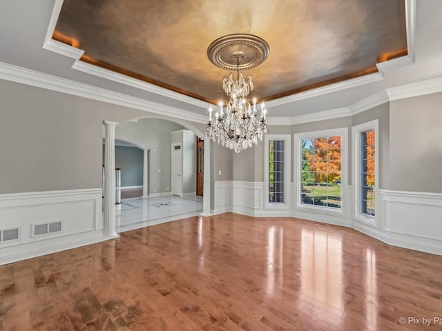 unfurnished dining area featuring ornamental molding, hardwood / wood-style floors, decorative columns, and a raised ceiling