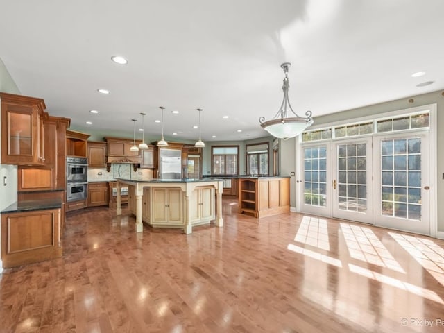 kitchen with a kitchen island, double oven, a kitchen breakfast bar, decorative light fixtures, and light hardwood / wood-style flooring