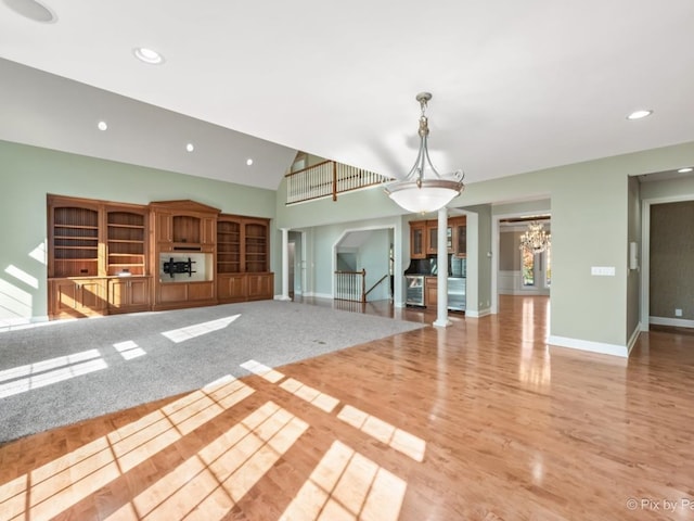 unfurnished living room with light hardwood / wood-style floors, a notable chandelier, and vaulted ceiling