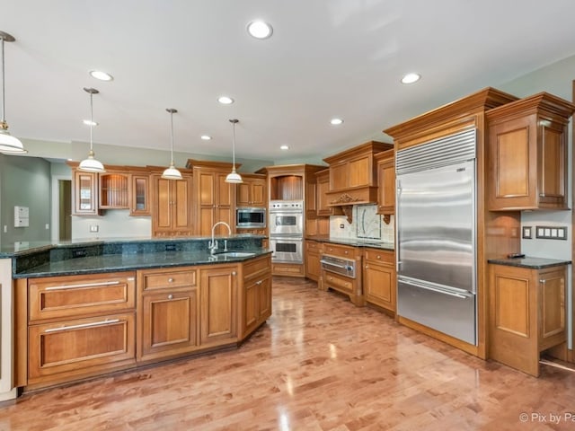 kitchen featuring built in appliances, light hardwood / wood-style floors, sink, and pendant lighting