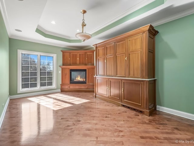 unfurnished living room with light hardwood / wood-style flooring, a tray ceiling, and crown molding