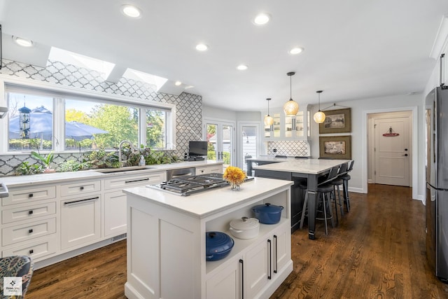 kitchen with tasteful backsplash, appliances with stainless steel finishes, white cabinets, a sink, and a center island