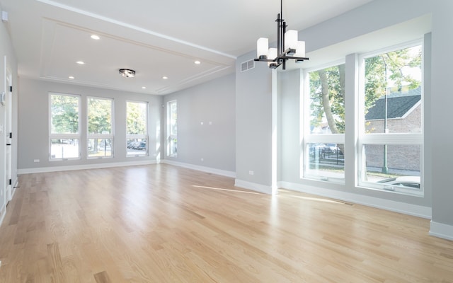 empty room with light hardwood / wood-style floors, a notable chandelier, and a healthy amount of sunlight