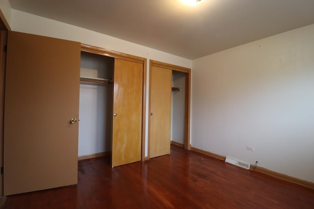 unfurnished bedroom with dark hardwood / wood-style floors and multiple closets