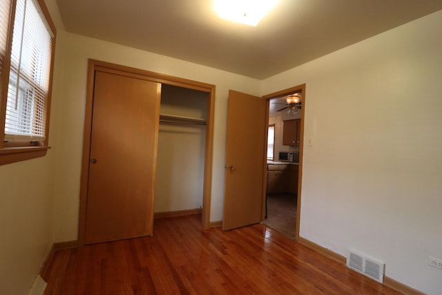 unfurnished bedroom featuring multiple windows, hardwood / wood-style floors, and a closet