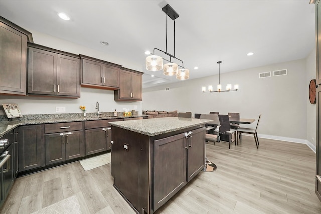 kitchen featuring dark brown cabinetry, light hardwood / wood-style floors, light stone counters, a center island, and pendant lighting