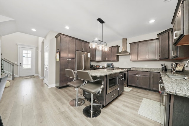 kitchen featuring sink, wall chimney range hood, pendant lighting, light wood-type flooring, and appliances with stainless steel finishes