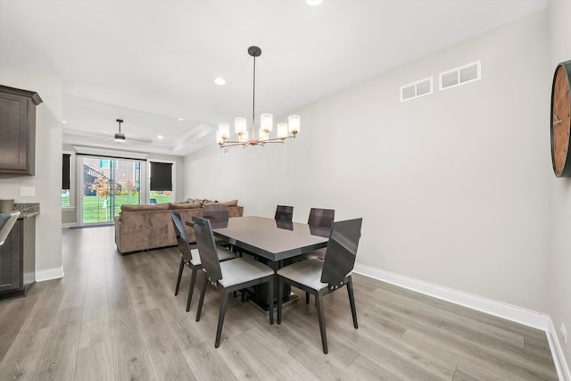 dining area with light hardwood / wood-style floors, ceiling fan with notable chandelier, and a tray ceiling