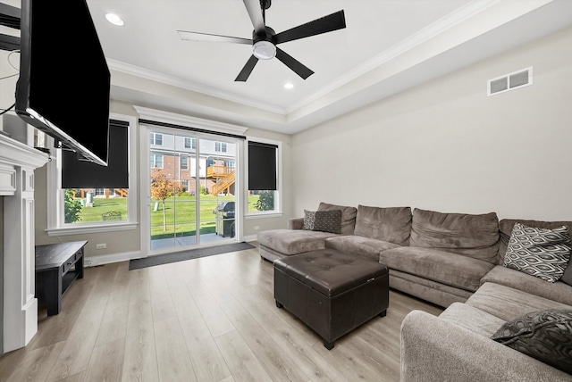 living room with ceiling fan, light hardwood / wood-style flooring, crown molding, and a tray ceiling