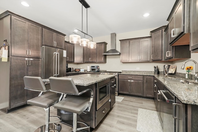 kitchen featuring sink, appliances with stainless steel finishes, light wood-type flooring, wall chimney range hood, and pendant lighting