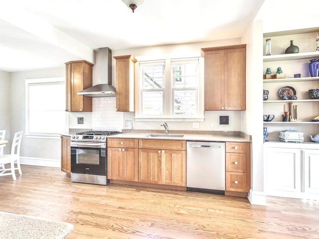 kitchen with appliances with stainless steel finishes, sink, wall chimney range hood, and light wood-type flooring