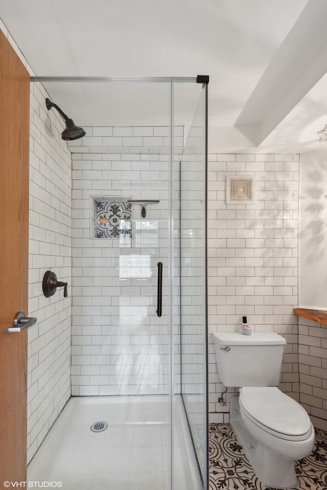 bathroom with a shower with door, toilet, tile patterned floors, and tile walls