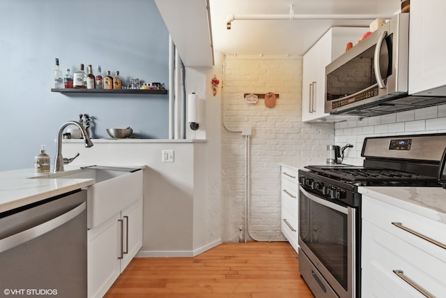 kitchen featuring light stone countertops, light hardwood / wood-style floors, stainless steel appliances, white cabinets, and decorative backsplash