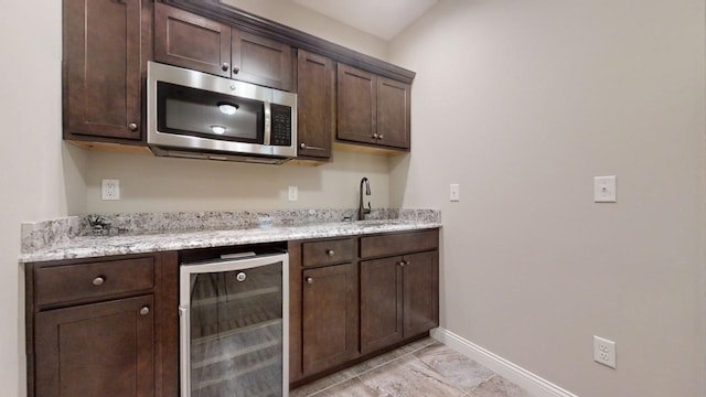 bar with light stone counters, beverage cooler, sink, and dark brown cabinets