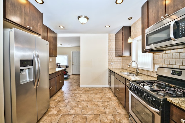 kitchen featuring hanging light fixtures, stainless steel appliances, sink, light stone counters, and tasteful backsplash