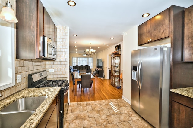 kitchen featuring tasteful backsplash, appliances with stainless steel finishes, an inviting chandelier, light stone countertops, and light wood-type flooring