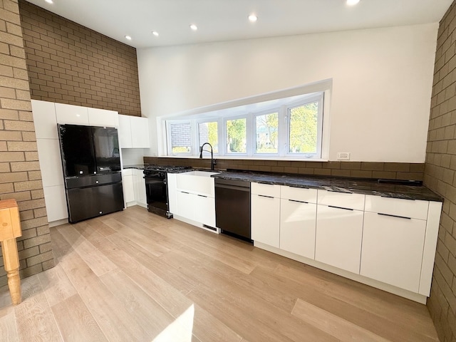 kitchen with lofted ceiling, dishwasher, black fridge, light wood-type flooring, and white cabinets