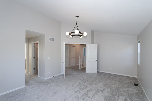 carpeted spare room featuring an inviting chandelier and lofted ceiling