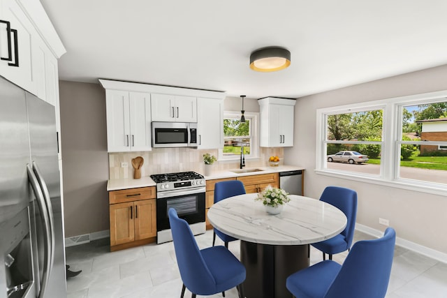 kitchen featuring sink, hanging light fixtures, stainless steel appliances, decorative backsplash, and white cabinets