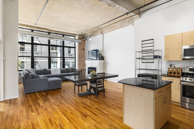 kitchen with light hardwood / wood-style floors, a center island, appliances with stainless steel finishes, light brown cabinets, and brick wall